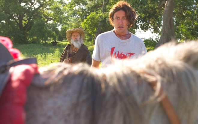 Jesuita Barbosa, caracterizado como seu personagem em Pantanal, está olhando para o cavalo com Osmar Prado, observando por trás