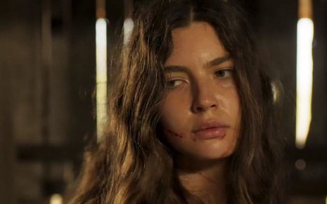 A atriz Alanis Guillen como Juma em Pantanal; ela está olhando para o lado com cara de desconfiada e a boca suja de sangue
