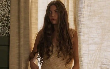 A atriz Alanis Guillen como Juma em Pantanal; ela está em frente a uma cortina, olhando para o lado com as mãos estendidas para baixo