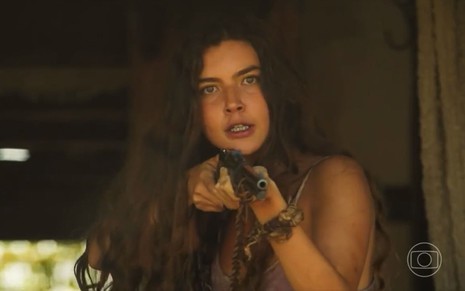 A atriz Alanis Guillen como Juma em Pantanal; ela está olhando para a frente, com uma espingarda apontada e cara de fúria
