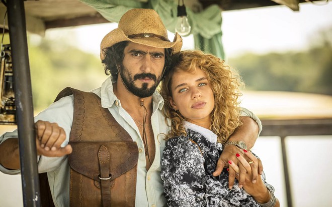 Renato Goés com uma camisa branca quadriculada e um chapéu de sertanejo junto com Bruna Linzmeyer nas gravações de Pantanal