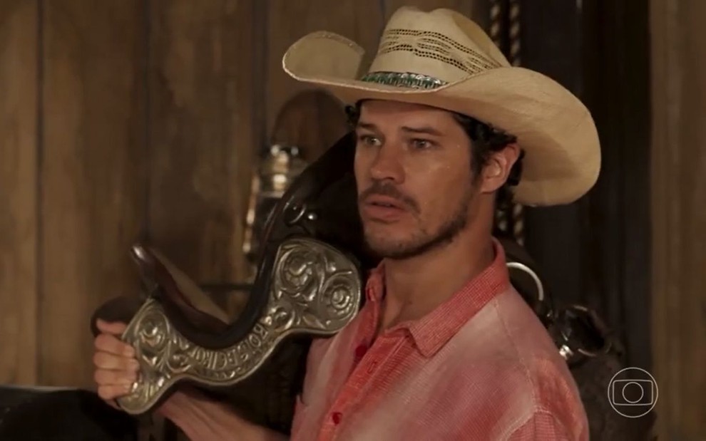 O ator José Loreto como Tadeu em Pantanal; ele está de chapéu e de lado, olhando para frente com cara séria enquanto segura a sela de prata