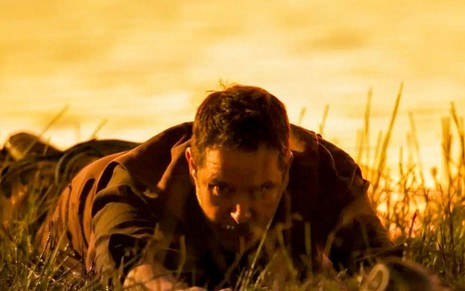 O ator Murilo Benício como Tenório em Pantanal; ele está deitado na grama, de bruços, olhando para baixo com cara de agoniado