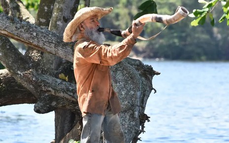 O ator Osmar Prado como Velho do Rio em Pantanal; ele está em pé, de lado, tocando o berrante