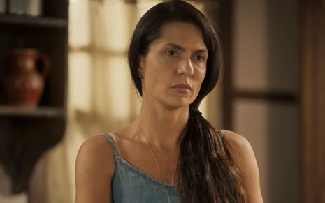 A atriz Paula Barbosa como Zefa em Pantanal; ela está em pé, olhando para frente com cara de desanimada e pensativa