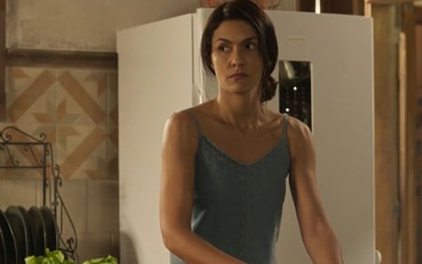 A atriz Paula Barbosa como Zefa em Pantanal; ela está em pé, olhando para o lado com as mãos dentro de uma bacia