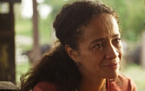 A atriz Aline Borges como Zuleica em Pantanal; ela está sentada, olhando para o lado com cara de choro