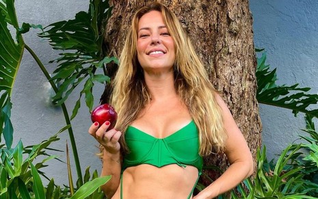Paolla Oliveira está de biquíni verde, com os cabelos soltos e segurando uma maçã