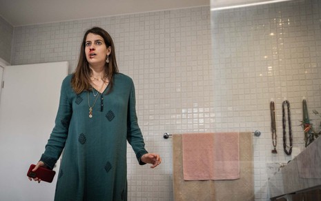 Maria Bopp está no banheiro, com um vestido esverdeado, celular na mão e o rosto ensanguentado em cena de As Seguidoras