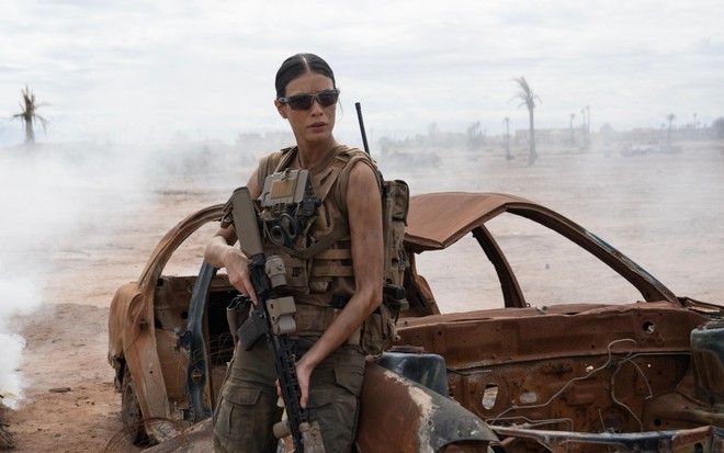 Laysla de Oliveira usa roupa de soldado, colete à prova de balas e óculos de sol em meio a cenário de guerra