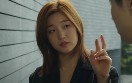 A atriz Park So Dam em cena do filme Parasita; ela levanta dois dedos da mão enquanto olha para o lado