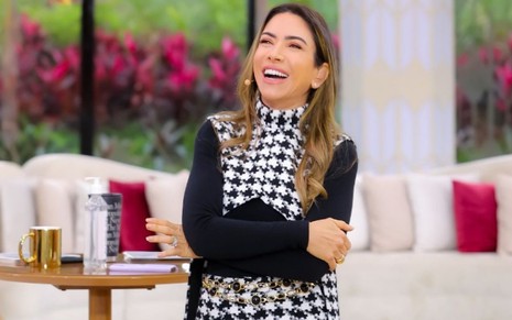 Patricia Abravanel de braços cruzados, rindo, com um vestido xadrez