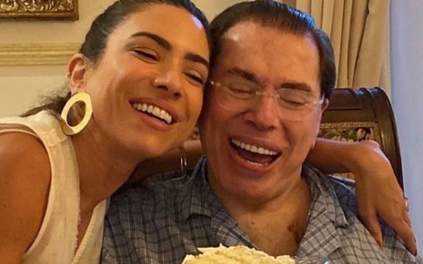 Patrícia Abravanel e Silvio Santos seguram um pedaço de bolo e riem