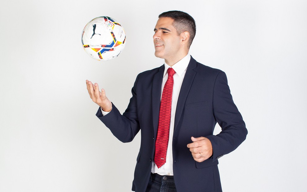 Paulo Andrade veste um paletó preto, com uma camisa branca e uma gravata vermelha. Ele segura uma bola e joga ela para cima nos estúdios da Disney.