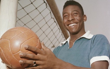 Pelé, ex-jogador do Santos e Brasil, segura bola e veste camiseta cinza com gola e mangas brancas