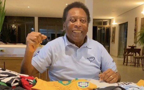 De pólo azul, Pelé sorri ao lado de camisas de times brasileiro