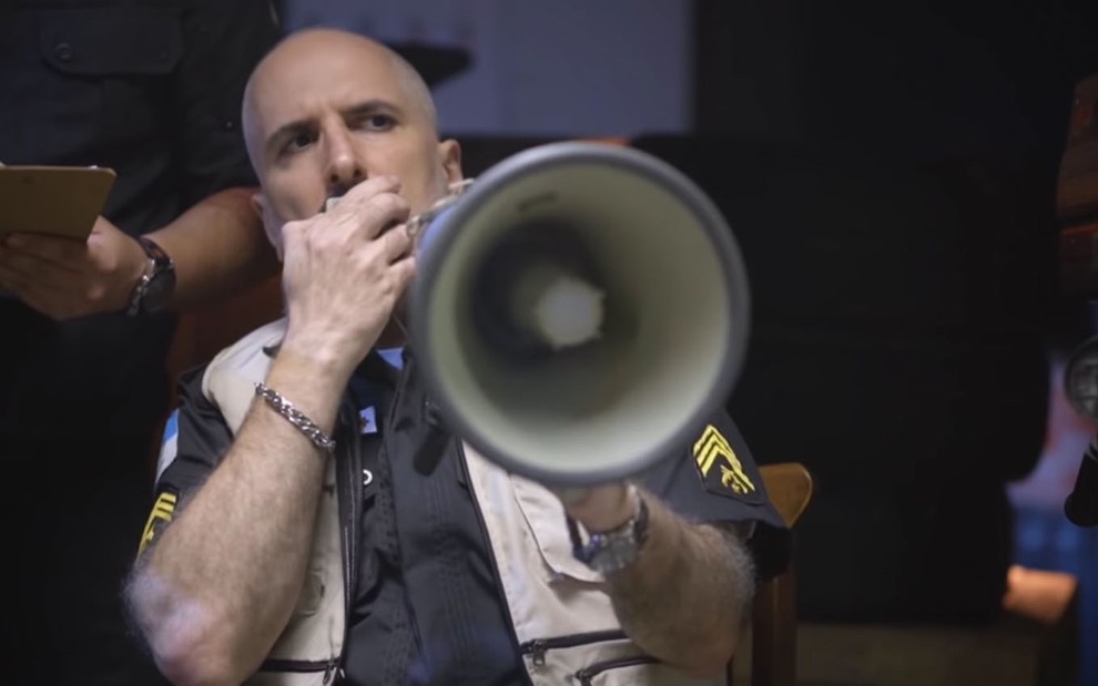 O ator Antonio Tabet caracterizado como o Peçanha com um megafone na mão em cena do vídeo Peçanha contra Juliette