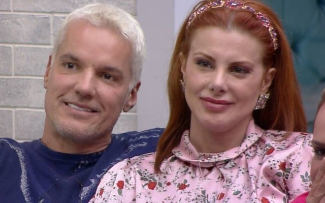 Bruno sorri, veste camiseta azul e está ao lado de Deborah; Deborah sorri, usa tiara rosa no cabelo e veste blusa rosa