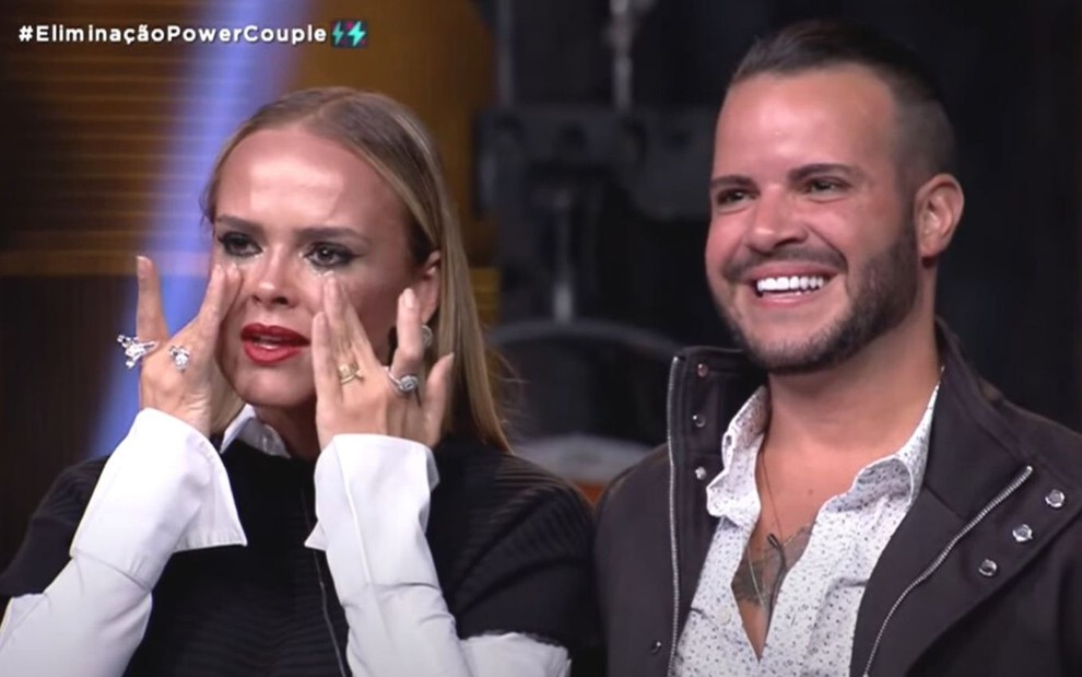 Nina seca as lágrimas enquanto Filipe Duarte sorri ao lado delas; casal foi eliminado do Power Couple Brasil