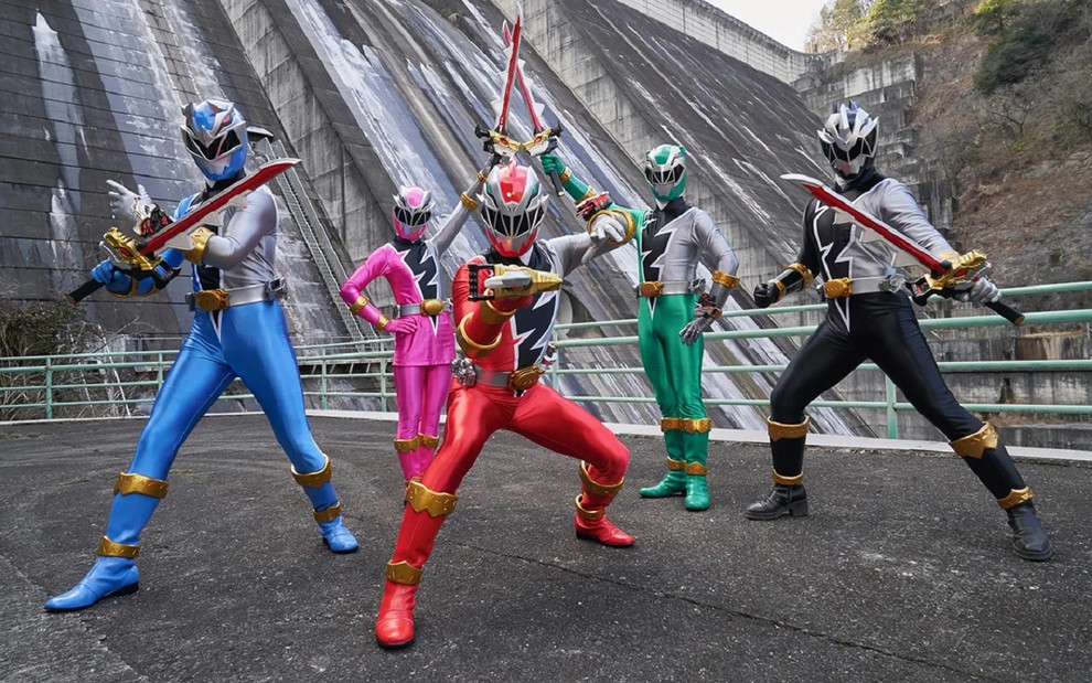 Elenco de Power Rangers Dino Fury.  Eles fazem pose com as armas e usam uniformes coloridos com as cores vermelha, verde, preta, rosa e azul.
