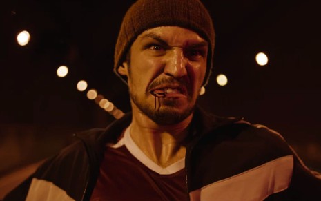Gabriel Leone tem expressão furiosa enquanto morde pino de granada em cena da série Dom