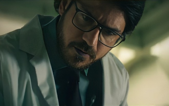 Marco Pigossi está caracterizado como cientista, com jaleco branco e óculos de nerd, em cena de Gen V