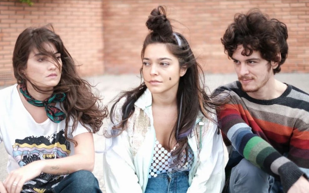 Foto promocional de Lov3 mostra Elen Clarice, Bella Camero e João Oliveira sentados em uma calçada