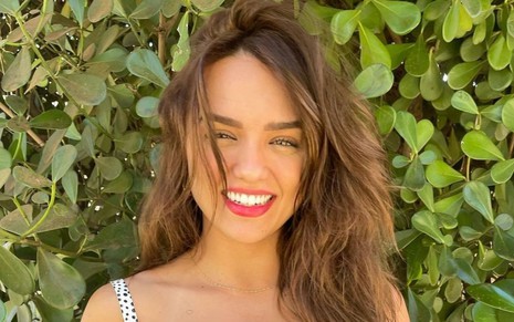 Rafa Kalimann está de cabelos soltos e sorri; ela posa em frente a uma parede de plantas em foto publicada no Instagram