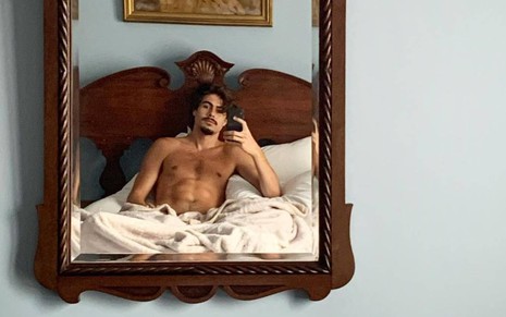 Rafael Vitti surge em espelho com um celular na mão, sem camisa e deitado em uma cama