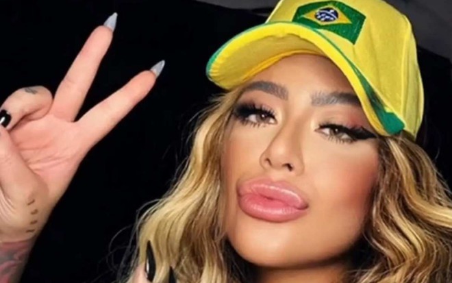 Rafaella Santos está com boné verde e amarelo e faz sinal com os dedos das mãos