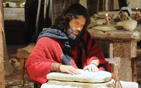 Guilherme Winter grava cena com expressão séria mexendo em tábuas, como Moisés em A Bíblia