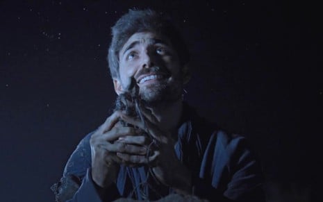 Miguel Coelho em cena de A Bíblia: ator segura animal nas mãos e olha para cima