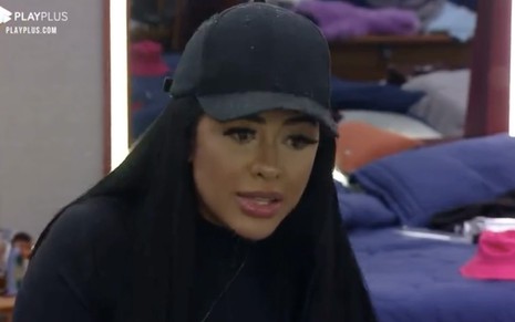 Fernanda Medrado com um boné preto e uma blusa preta, de olhos levemente arregalados, olha para esquerda