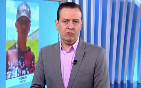 O apresentador e jornalista Celso Zucatelli olha sério no Balanço Geral de sábado (22) na Record; um rapaz aparece no telão do telejornal atrás do apresentador