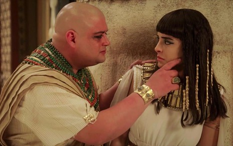 Ricardo Lyra e Letícia Almeida em cena de Gênesis, ator segura o rosto da parceira de cena; ambos estão caracterizados como moradores do Egito antigo