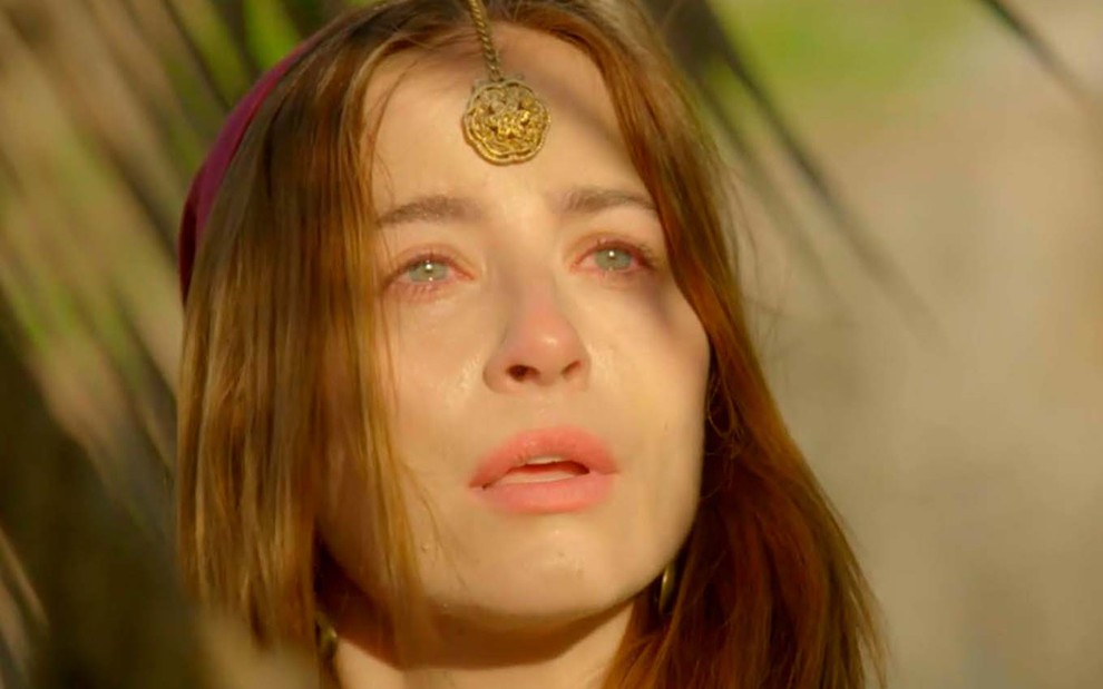 A atriz Barbara França olha para cima, como se falasse com Deus, com lágrimas nos olhos e caracterizada como Rebeca em cena de Gênesis