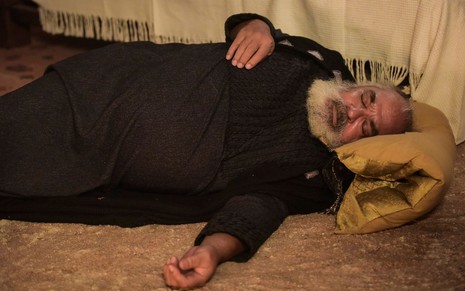 Roberto Bomfim caracterizado como Betuel em cena de Gênesis: ator está deitado e de olhos fechados no chão