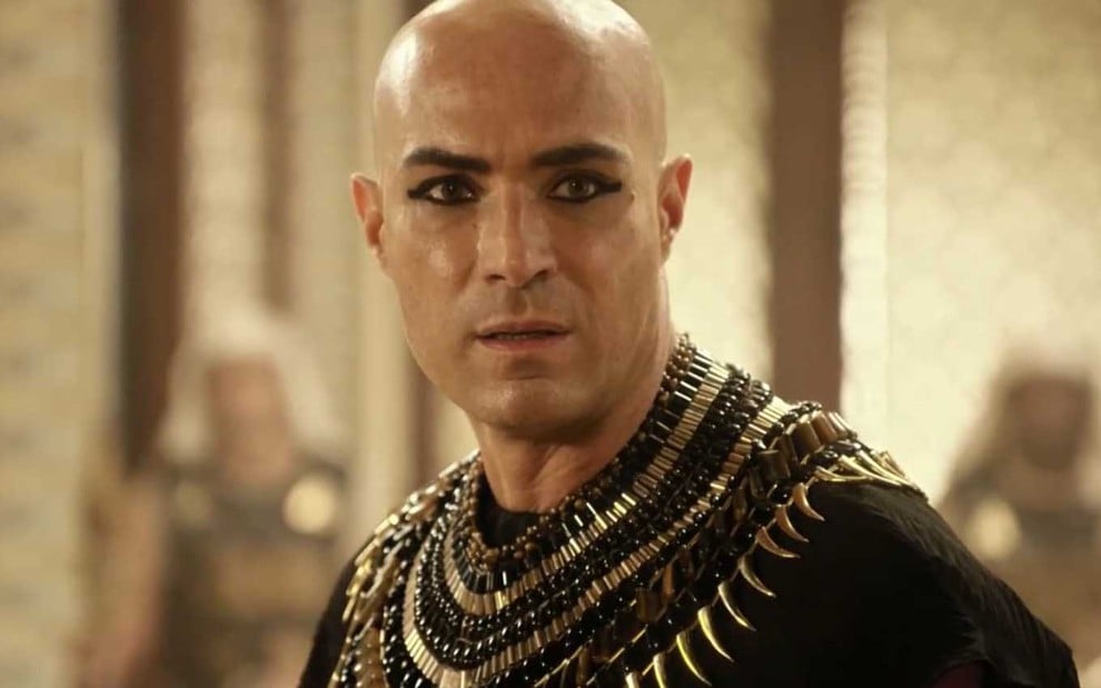 O ator Fernando Pavão de cabelos raspados e kajal nos olhos com expressão de preocupação como o faraó Sheshi em cena de Gênesis