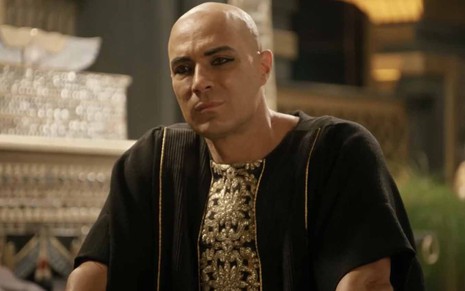 O ator Fernando Pavão como o faraó Sheshi vestido de preto, em sinal de luto, com expressão séria em cena de Gênesis