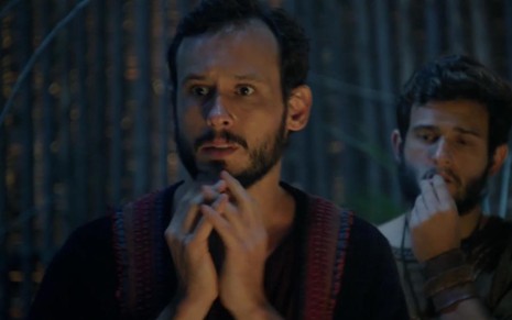 O ator Guilherme Dellorto leva as mãos entrelaçadas ao queixo, em sinal de desespero, como Isaque em cena noturna de Gênesis