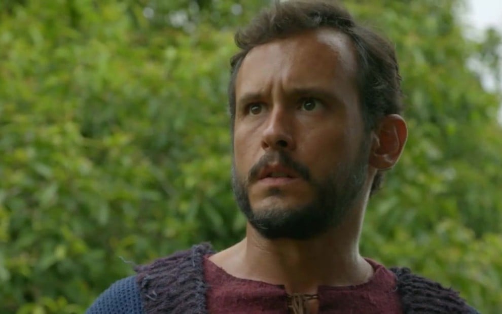 Guilherme Dellorto em cena de Gênesis: ator está caracterizado com Isaque, e olha para alguém fora do quadro com surpresa
