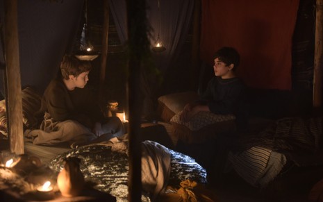 Enzo Barone e Breno Moraes gravam sentados em tenda iluminada por velas como Jacó e Esaú de Gênesis