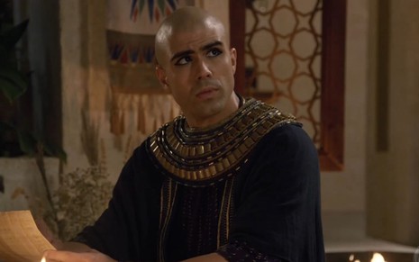 Juliano Laham em cena de Gênesis: ator está caracterizado com túnica com detalhes dourados e olha para alguém fora do quadro