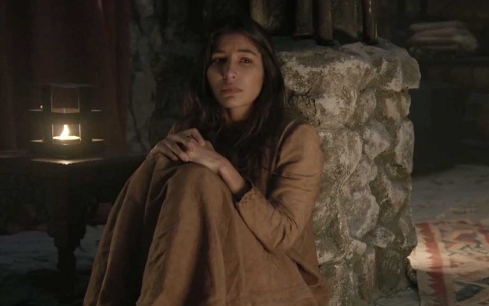 A atriz Juliana Xavier está sentada no chão, com expressão de choro, como a Tamar em cena noturna de Gênesis