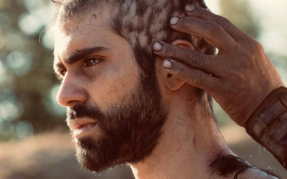 De perfil, o ator Juliano Laham como José tem os cabelos raspados com uma lâmina de vidro em cena de Gênesis
