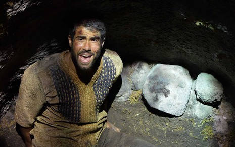 O ator Juliano Laham com o rosto machucado e bastante sujo está sentado no fundo de uma cisterna vazia em cena de Gênesis