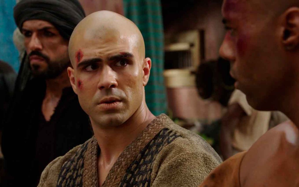 O ator Juliano Laham com a cabeça careca e um machucado no supercílio direto como José, em expressão de dúvida, em cena de Gênesis