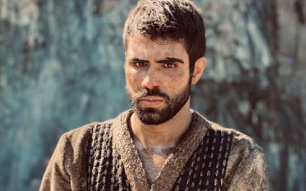 O ator Juliano Laham com expressão sofrida e rosto machucado como José em cena de Gênesis