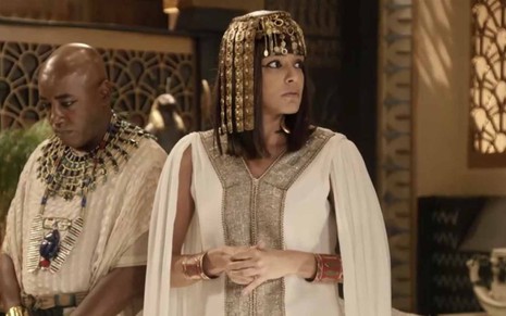 A atriz Kizi Vaz está com as mãos em frente ao corpo, entrelaçadas, e olha com surpresa para a direita como a Amarilis em cena de Gênesis