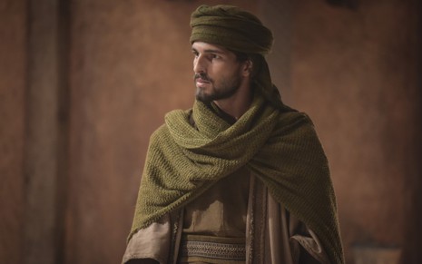 Brenno Leone grava com turbante e lenço verde olhando para alguém com expressão séria como Labão de Gênesis